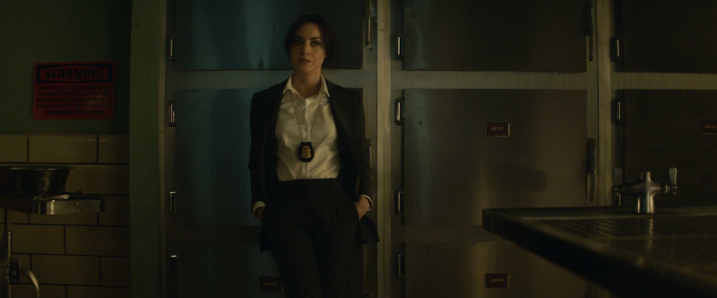 Rio Vidal (Aubrey Plaza) posing in a morgue, wearing a police badge and start attire, in Agatha All Along