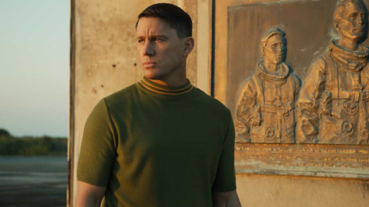 Channing Tatum as Cole Davis in Fly Me to the Moon, wearing a green sweater, standing at the Apollo 1 launch site, staring outwards