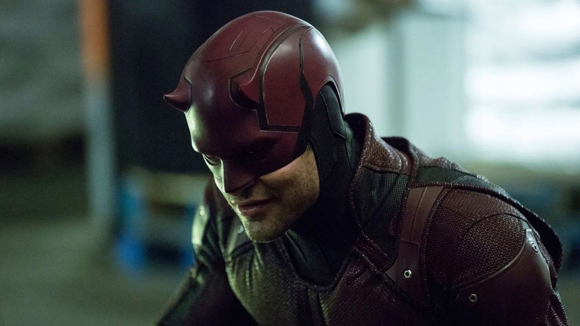 A person wearing a maroon and black armored suit with a helmet featuring small horns, the Marvel character Daredevil.
