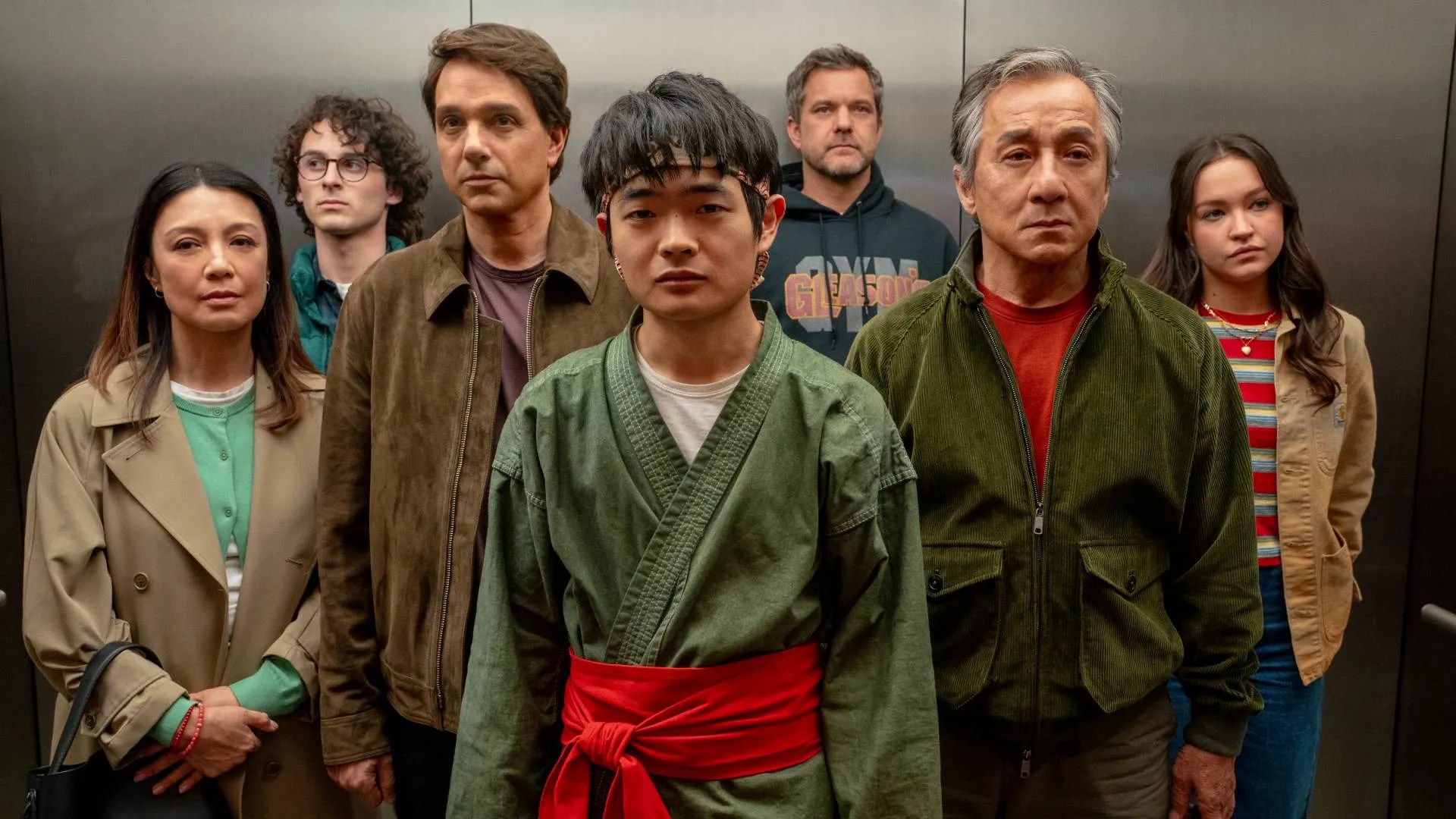 Jackie Chan, Ben Wang, and Ralph Macchio stand side by side in the promotional poster for Karate Kid Legends, dressed in casual attire against a cinematic background.
